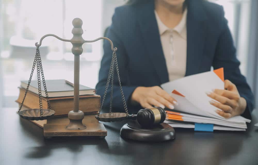 Image is of a lawyer reviewing legal documents beside scales of justice, concept of a criminal defense lawyer preparing a defense strategy