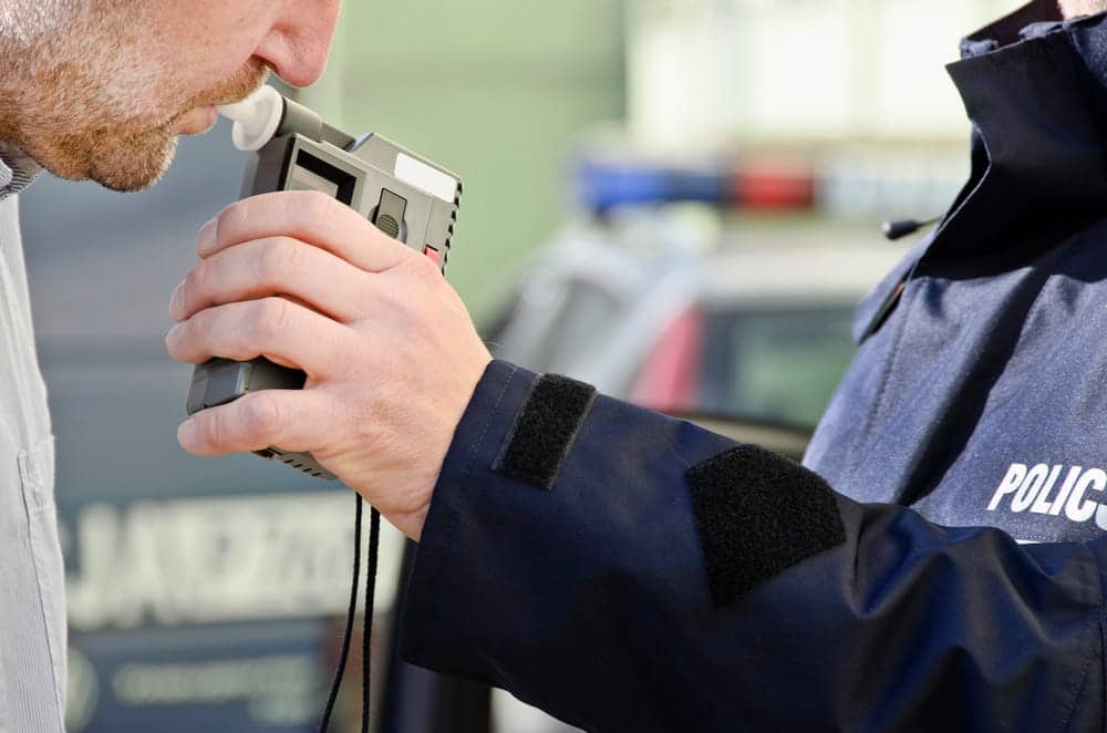 Image is of a driver taking a breath test administered by police, concept of a DUI lawyer reviewing roadside testing procedures